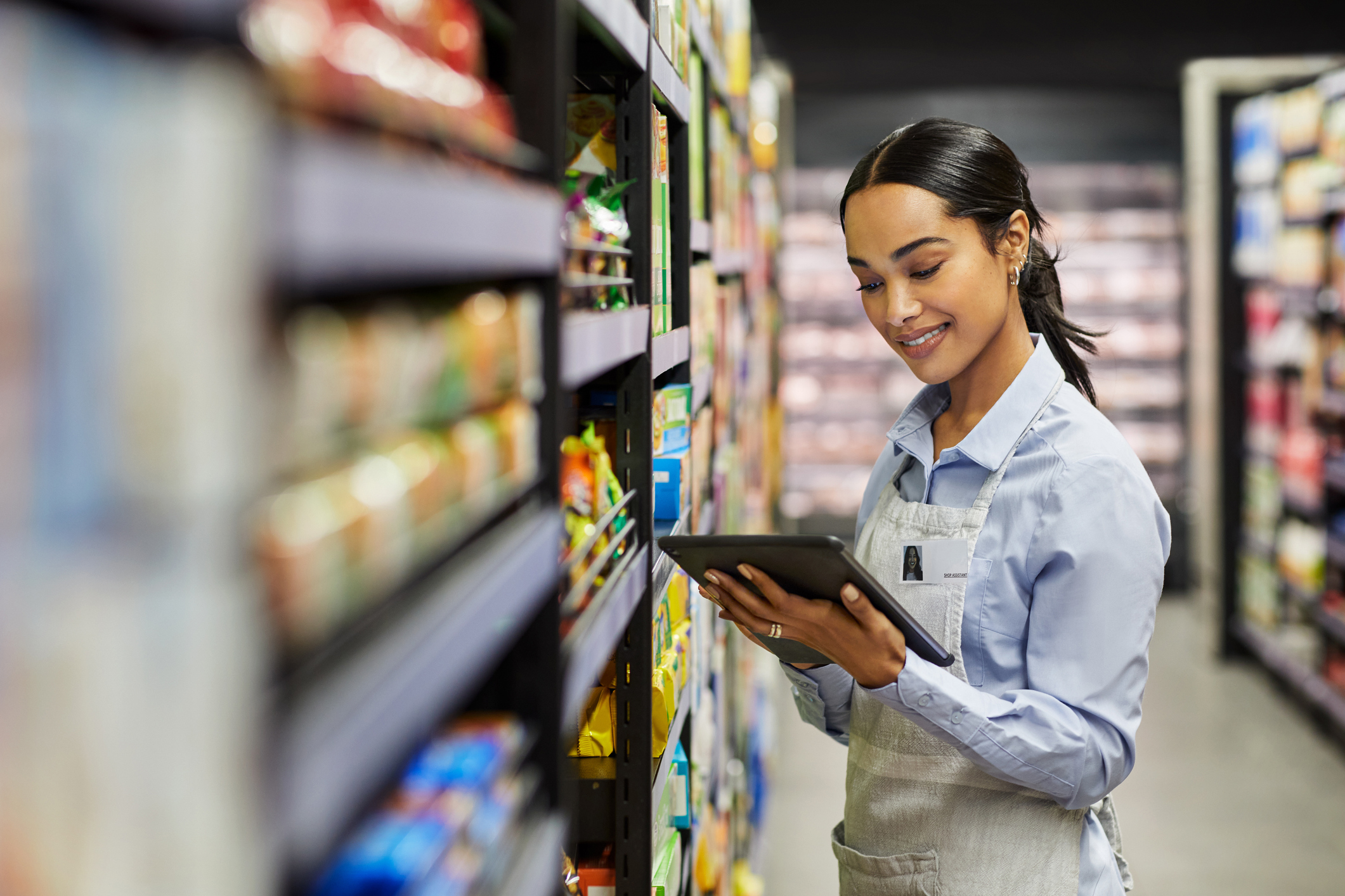 Store employee checking inventory on a tablet in a supermarket aisle, illustrating retail negotiation challenges